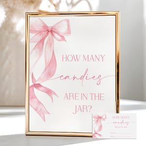 May include: A framed sign with a gold border and pink text that reads "HOW MANY candies ARE IN THE JAR?" A watercolor bow and ribbon design is on the sign. A smaller card with the same design is also present.