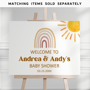 May include: Welcome to Andrea & Andy's Baby Shower sign with a rainbow and sun illustration. The sign is white with brown text and a date of 03.23.20XX.