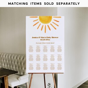 May include: A white seating chart with a yellow sun graphic at the top. The text reads "Jessica & Matt's Baby Shower 02.20.20xx Please Find Your Seat". The chart lists tables with guest names.