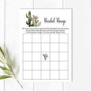 May include: A printable bridal shower bingo card with a cactus theme. The card has a 5x5 grid with squares to fill in with gifts the bride-to-be will receive. The text "Bridal Bingo" is at the top of the card.