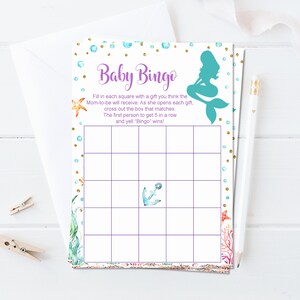 May include: A printable baby shower bingo card with a mermaid illustration and a purple and gold design. The card has a grid with squares to fill in with gifts the mom-to-be will receive. The text reads "Baby Bingo" and includes instructions for playing the game.