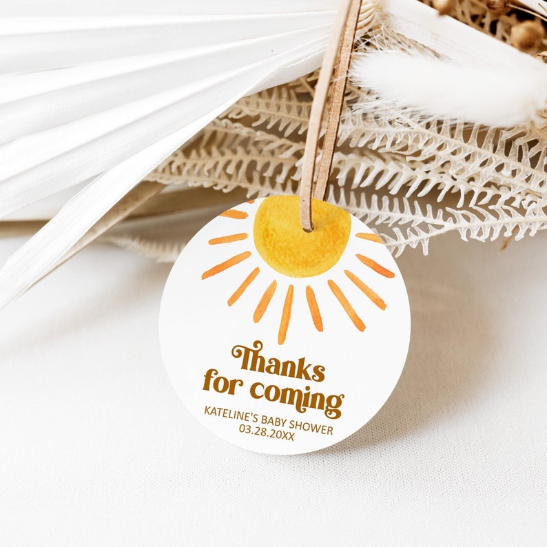 May include: Round white thank you tag with a yellow sun and orange rays. The text reads "Thanks for coming" with the words "KATELINE'S BABY SHOWER 03.28.20XX" below.