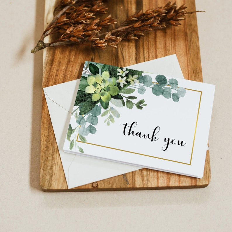 May include: A white thank you card with a gold frame and a watercolor illustration of green succulents and leaves. The text "thank you" is written in black cursive lettering.
