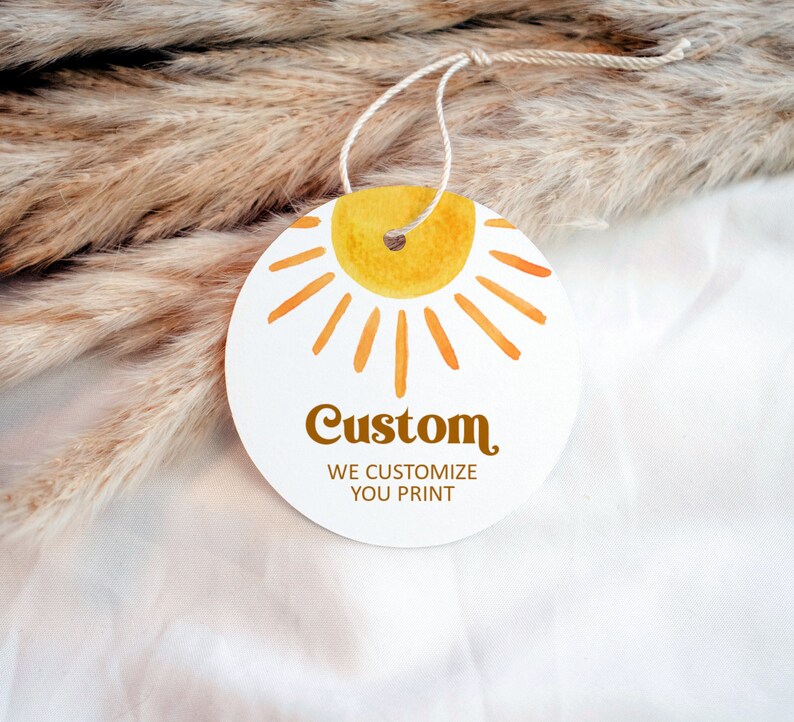 May include: A round white tag with a yellow sun graphic and the text "Custom We Customize You Print". The tag is attached to a string.