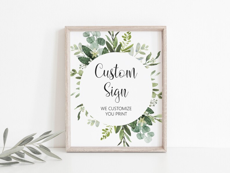 May include: A framed sign with a white background and a circle of green leaves. The text on the sign reads 'Custom Sign' and 'We Customize You Print'.