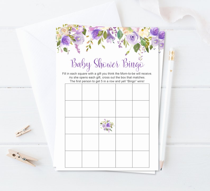 Puede incluir: Juego de bingo para baby shower con un dise&ntilde;o floral en tonos morados, lavanda y blanco. El juego incluye instrucciones y una cuadr&iacute;cula para jugar. Tambi&eacute;n se ven un l&aacute;piz y pinzas para la ropa.