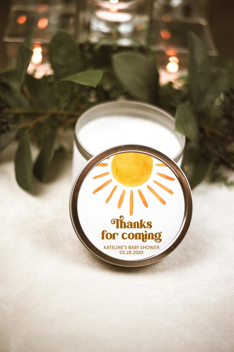 May include: A white candle in a silver tin with a yellow sun and orange rays graphic. The label reads "Thanks for coming" with the text "KATELINE'S BABY SHOWER 03.28.20XX" below.