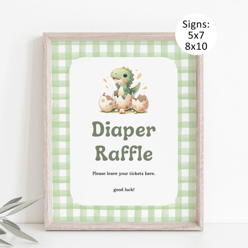 May include: A framed sign with a green gingham border and a white centre. The centre features a watercolour illustration of a baby dinosaur hatching from an egg. Text reads "Diaper Raffle" and "Please leave your tickets here. good luck!" Sizes: 5x7 and 8x10.