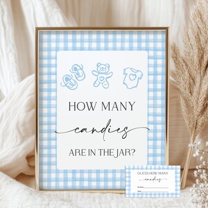 May include: A framed sign with a blue and white gingham background. The sign reads "HOW MANY candies ARE IN THE JAR?" with baby-themed illustrations. A matching guess card is included.