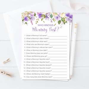 Puede incluir: Una tarjeta blanca con el texto "WHO KNOWS Mommy Best?" en escritura morada, con preguntas debajo. La tarjeta est&aacute; decorada con elementos florales de acuarela en tonos morados y blancos. Un l&aacute;piz y un sobre est&aacute;n al lado de la tarjeta.