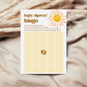 K&ouml;nnte beinhalten: Eine gelbe und braune Babyparty-Bingo-Karte mit einem Sonnen-Motiv und dem Text "baby shower bingo". Die Karte hat ein Raster mit Feldern, in einem der Felder befindet sich ein Fu&szlig;abdruck-Motiv. Der Text unter dem Raster lautet "F&uuml;lle jedes Feld mit einem Geschenk, von dem du glaubst, dass die werdende Mutter es erhalten wird. Wenn sie jedes Geschenk &ouml;ffnet, streiche das entsprechende Feld durch. Die erste Person, die 5 in einer Reihe erh&auml;lt und "Bingo" ruft, gewinnt!"