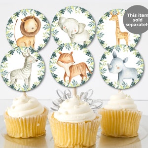 May include: Cupcakes with toppers featuring watercolor illustrations of safari animals, including a lion, elephant, giraffe, zebra, tiger, and rhino. The toppers are surrounded by a green leaf border. The cupcakes have white frosting.