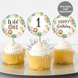 May include: Three cupcake toppers with a jungle animal theme. The toppers feature a green leafy background with a lion, giraffe, zebra, monkey, and elephant. The toppers say "Wild One", "1", and "Happy Birthday".
