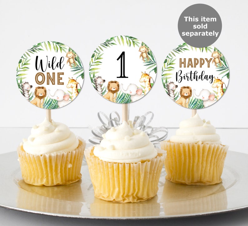May include: Three cupcake toppers with a jungle animal theme. The toppers feature a green leafy background with a lion, giraffe, zebra, monkey, and elephant. The toppers say "Wild One", "1", and "Happy Birthday".