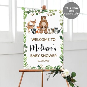 May include: Welcome to Melissa's Baby Shower sign with a woodland theme. The sign features a brown bear, a deer, a fox, a raccoon, and other woodland animals. The sign is decorated with green leaves and a white background.