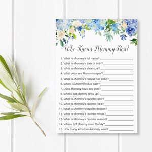 May include: A baby shower game card titled "Who Knows Mommy Best?" features a floral design with blue and white flowers. The card includes fill-in-the-blank questions about the mother-to-be, such as her favorite color and movie.