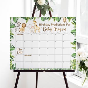 May include: A white calendar with a jungle theme, featuring illustrations of a zebra, lion, elephant, giraffe, and monkey. The calendar is for "Baby Grayson" with the text "Birthday Predictions For." It is displayed on a wooden easel.