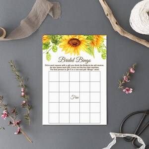 May include: A printable bridal bingo card with a sunflower illustration. The card has a 5x5 grid with squares to fill in with gifts the bride-to-be will receive. The text on the card reads "Bridal Bingo" and includes instructions for playing the game.