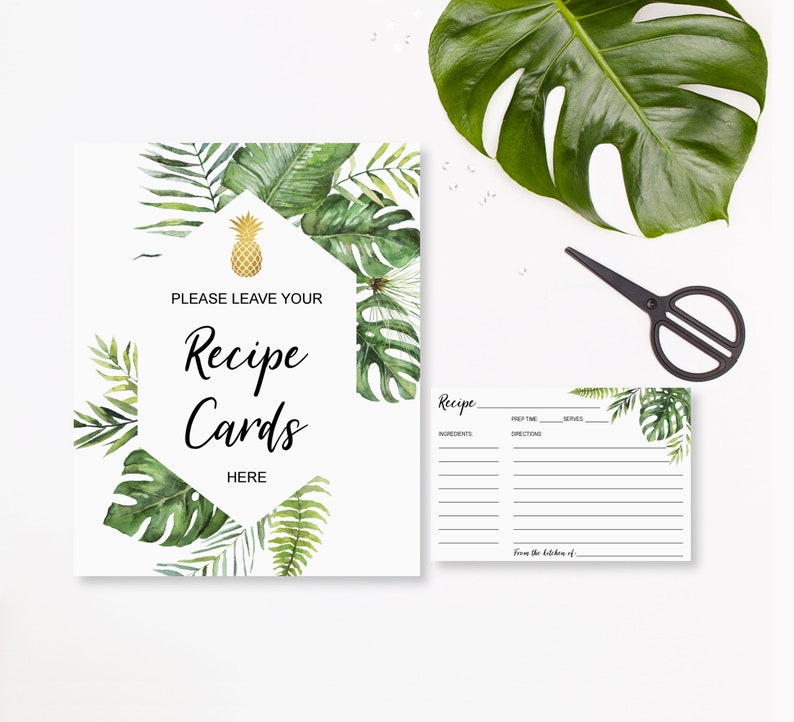 May include: White recipe card sign with tropical leaf and pineapple accents. The sign reads "PLEASE LEAVE YOUR Recipe Cards HERE." A matching recipe card is also present, along with black scissors and a large green leaf.