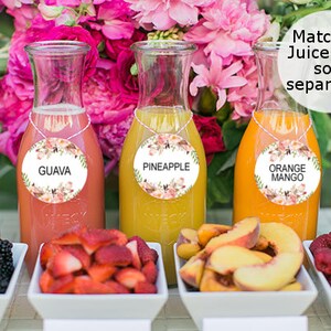 Pode incluir: Uma mesa com cinco garrafas de vidro cheias de sucos de diferentes cores. Cada garrafa tem uma etiqueta redonda com um design floral e o nome do suco: Laranja, Goiaba, Abacaxi, Manga Laranja e Cranberry. H&aacute; tigelas de frutas na frente de cada garrafa: amoras, morangos, fatias de p&ecirc;ssego e framboesas.