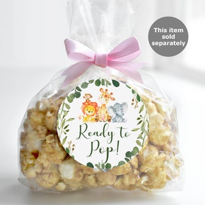 May include: A clear plastic bag filled with popcorn and a round sticker with a green leafy border. The sticker has a cartoon illustration of a lion, giraffe, and elephant. The text on the sticker reads "Ready to Pop!"