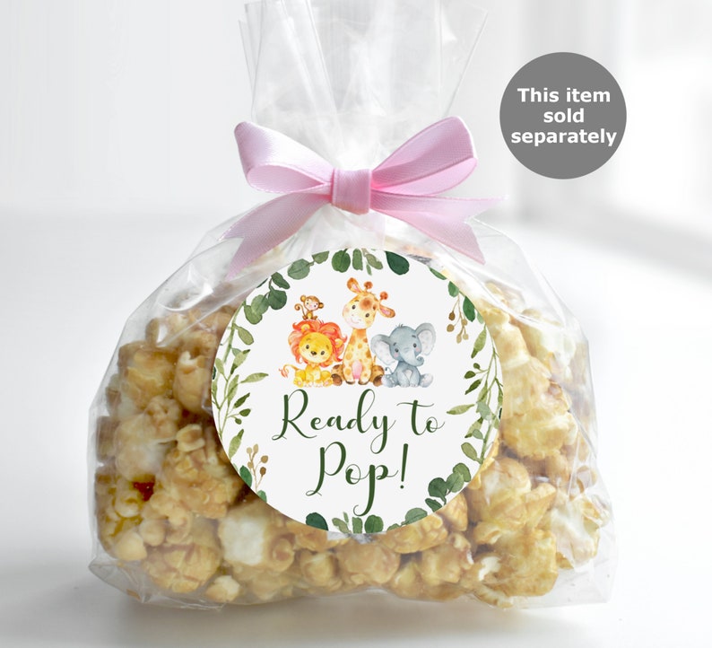 May include: A clear plastic bag filled with popcorn and a round sticker with a green leafy border. The sticker has a cartoon illustration of a lion, giraffe, and elephant. The text on the sticker reads "Ready to Pop!"