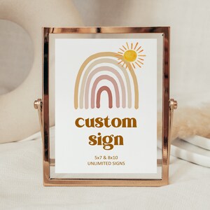 May include: A gold-framed sign with a rainbow and sun design. The text on the sign reads "custom sign 5x7 & 8x10 UNLIMITED SIGNS".