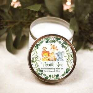 May include: A white candle in a tin container with a green, leafy, and animal-themed label. The label says "Thank You for celebrating with us! Love, Megan & Oliver".