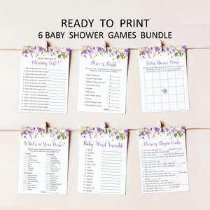 Puede incluir: Seis juegos de baby shower impresos en tarjetas blancas, sujetas con pinzas de madera en una cuerda. Las tarjetas presentan dise&ntilde;os florales morados y t&iacute;tulos de juegos como "&iquest;Qui&eacute;n conoce mejor a mam&aacute;?" y "El precio es correcto".