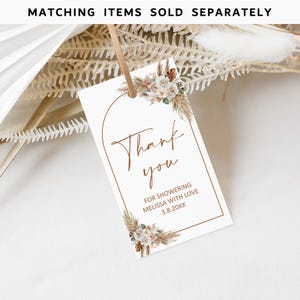 May include: A white thank you tag with a brown arch and floral design. The text reads "Thank you for showering Melissa with love 3.8.20XX".