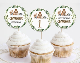 May include: Three cupcakes with white frosting, each topped with a round topper. The toppers feature woodland animal illustrations and text that reads "Grayson's 1st Birthday" and "Happy Birthday Grayson's".