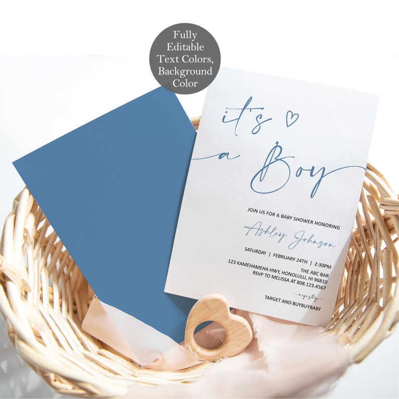 Op de afbeelding: Babyborrel uitnodiging met de tekst "It's a Boy" in blauw script. De uitnodiging staat op wit karton, met een blauwe envelop. Een houten hartvormig speeltje en een roze lint liggen in een gevlochten mand.