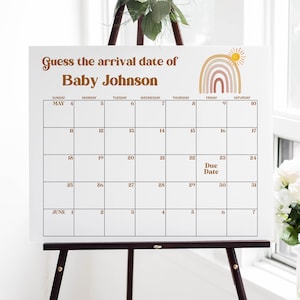 May include: A white board with a calendar on it. The calendar is for May and June. The title of the calendar is "Guess the arrival date of Baby Johnson". There is a rainbow with a sun above it in the top right corner.