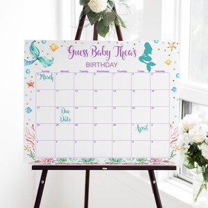 May include: A white calendar with a purple and teal mermaid design. The calendar is for the month of March and April. The text "Guess Baby Thea's Birthday" is at the top of the calendar.