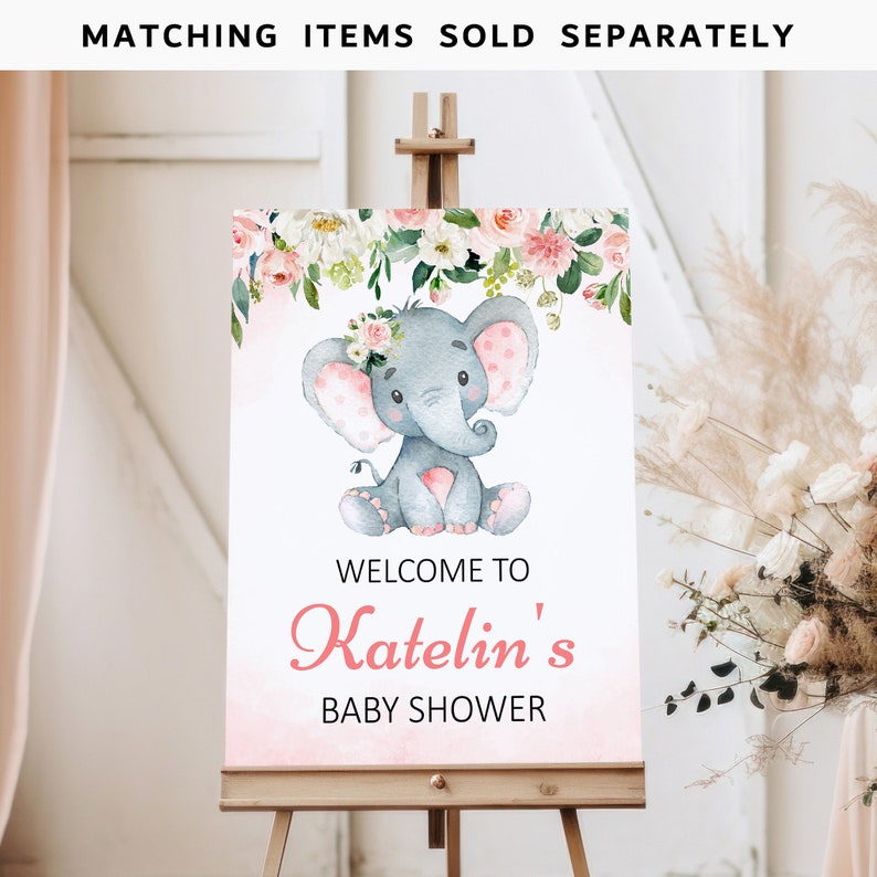 May include: A pink and white welcome sign with a floral garland and a gray elephant with pink polka dots. The sign says "Welcome to Katelin's Baby Shower".