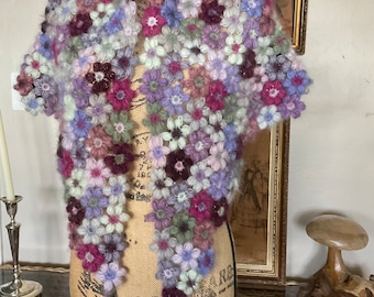 May include: A crocheted scarf with a floral design in shades of purple, pink, and white. The scarf is displayed on a mannequin.