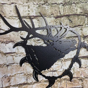 Op de afbeelding: Zwarte metalen wandkunst met een eland met grote geweien. De eland is omringd door een cirkel van scherpe punten.