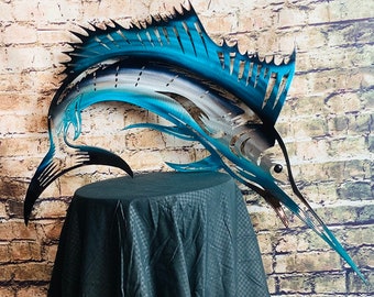 Puede incluir: Una escultura de marlin de metal azul y plateado con un pico largo y puntiagudo. La escultura está montada en una mesa negra y se coloca contra una pared de ladrillo.