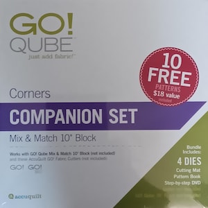 May include: A purple and white box with the text "GO! QUBE just add fabric!" and "Corners COMPANION SET Mix & Match 10" Block". The box includes 10 free patterns, 4 dies, a cutting mat, a pattern book, and a step-by-step DVD.