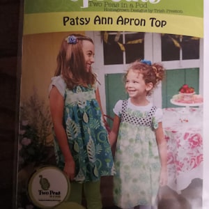 May include: A sewing pattern for a child's apron top called "Patsy Ann Apron Top" from the company "Two Peas in a Pod". The pattern includes instructions for a matching doll apron.