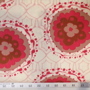 May include: White fabric with a repeating pattern of pink and brown stylized flowers. The flowers are surrounded by a pink and white dotted circle.