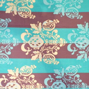May include: A teal and brown striped fabric with a repeating pattern of stylized pomegranates and floral designs. The pattern is in a light beige color.