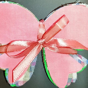 May include: A pink fabric butterfly with a pink and white ribbon bow. The butterfly is made of multiple layers of fabric and has a layered, ruffled edge.