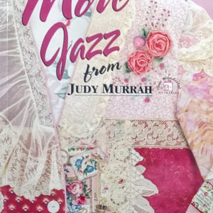 May include: A book cover titled "More Jazz from Judy Murrah" featuring a patchwork jacket design. The cover has a pink and white color scheme with floral and lace details. The text "New Shapes & Great Ideas for Wonderful Wearable Art" is at the bottom.