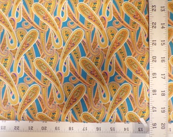 May include: Teal fabric with a paisley pattern in gold, orange, and white. The fabric is measured with a ruler in inches.