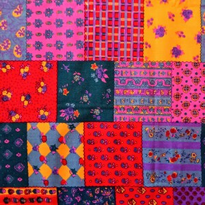 May include: A patchwork textile featuring a variety of patterned squares in vibrant colors. The design includes floral, geometric, and plaid patterns in shades of red, pink, purple, teal, and yellow. The fabric is likely cotton or a similar material.