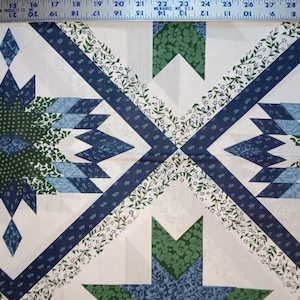 May include: A close-up of a quilt with a geometric pattern. The design features white, navy blue, light blue, and green shapes. The quilt has a repeating pattern of diamond and arrow-like shapes.