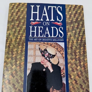 May include: A book titled "Hats on Heads: The Art of Creative Millinery" with a blue cover and a photo of a person wearing a hat. The book has a woven pattern on the cover and the author's name is Mildred Anlezark.