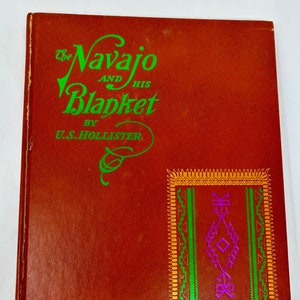 May include: The cover of a book titled "The Navajo and His Blanket" by U.S. Hollister. The cover is a deep red color with a green and gold design of a Navajo blanket.