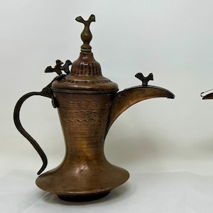 May include: Two antique copper coffee pots with ornate handles and spouts. The pots have intricate designs and are topped with finials.